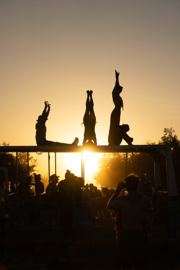 Four individuals hold yoga poses on a raised platform with a sunset in the background. Their silhouetted bodies spell the letters "LIB".