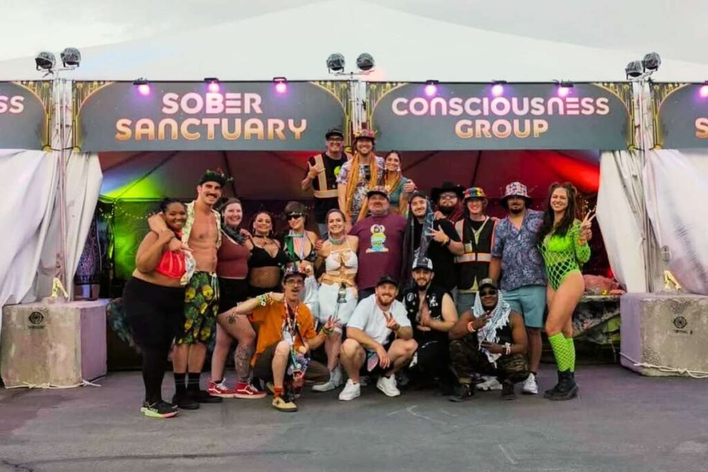 Volunteers and attendees stand in front of the Consciosness Group meeting tent at EDC Las Vegas 2025.
