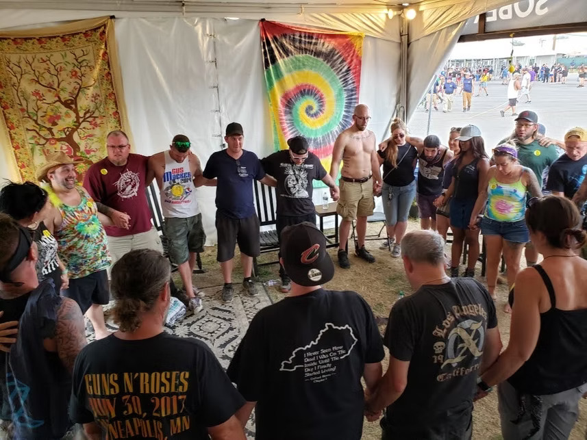 Inside the harmonium tent, volunteers hold hands to recite the serenity prayer as they close the meeting.